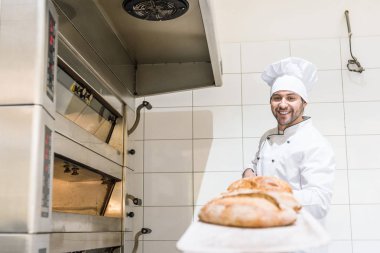 Baker holding Yönetim Kurulu sıcak taze ekmek ile Beyaz şefler şapkalı gülümseyen