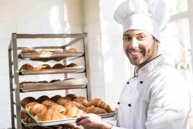 Baker holding tepsi ile ekmek fırınları taze pişmiş kruvasanlar gülümseyen