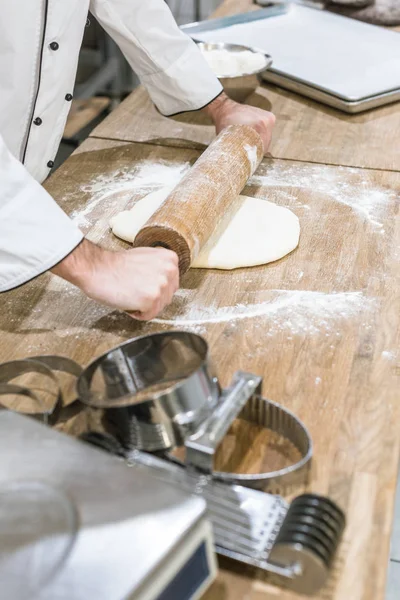 密切面包师的手推出未煮熟的面团在木桌上 — 图库照片