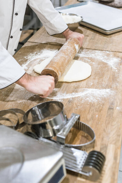 close up of baker hands rolling out uncooked dough on wooden table