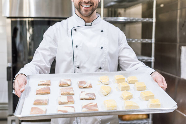 cropped view of smiling cook holding baking tray with raw dough