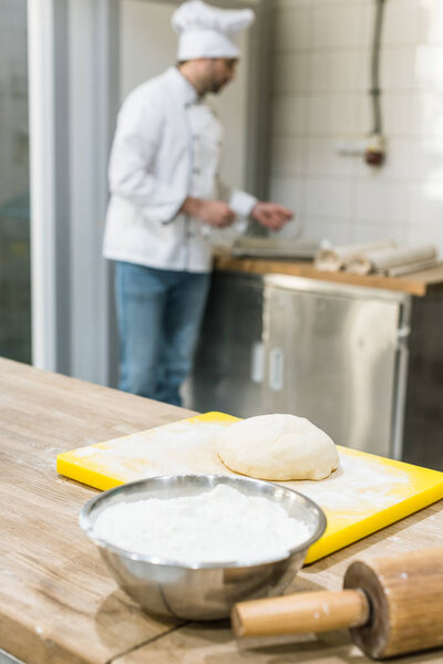 adult baker in chefs uniform preparing dough at counter
