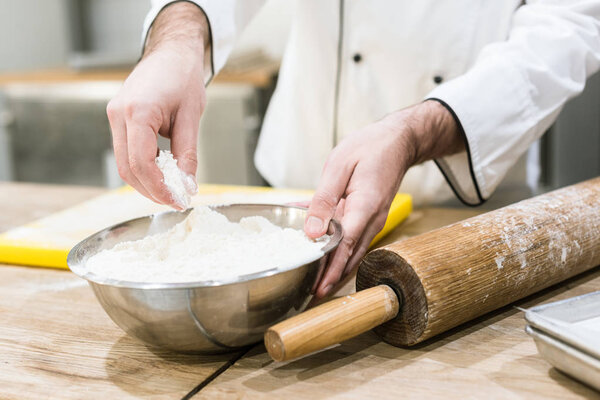 close up of baker holding bowl of flour at wooden counter