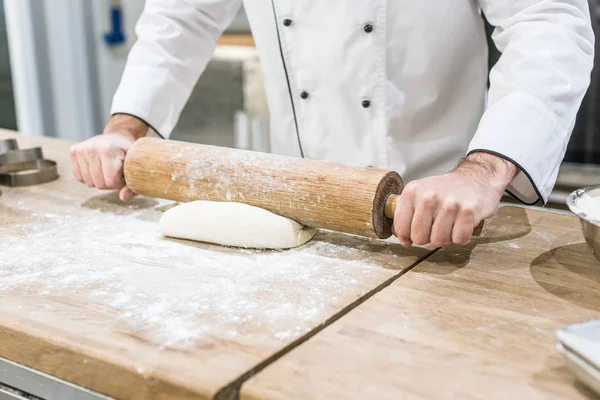 close up of chef hands rolling out dough on wooden table