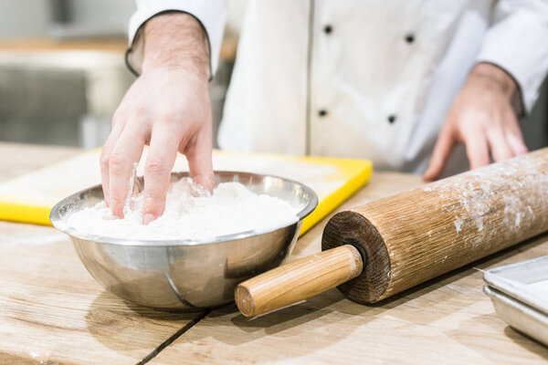 close up of baker hands with dough in metal bowl in bakehouse