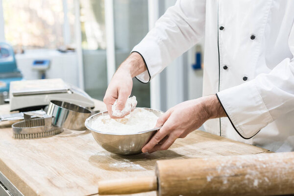 Cropped view of baker holding metal bowl with flour