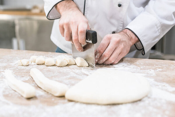 close up of chefs hands separating dough with cutter on wooden table