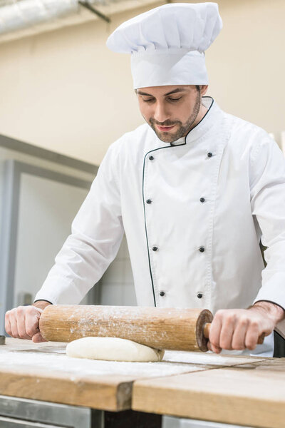 Handsome baker rolling out dough on wooden table