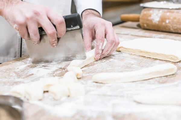 close up of baker hands cutting dough on wooden table