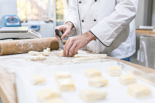 Cropped view of baker hands cutting dough on table