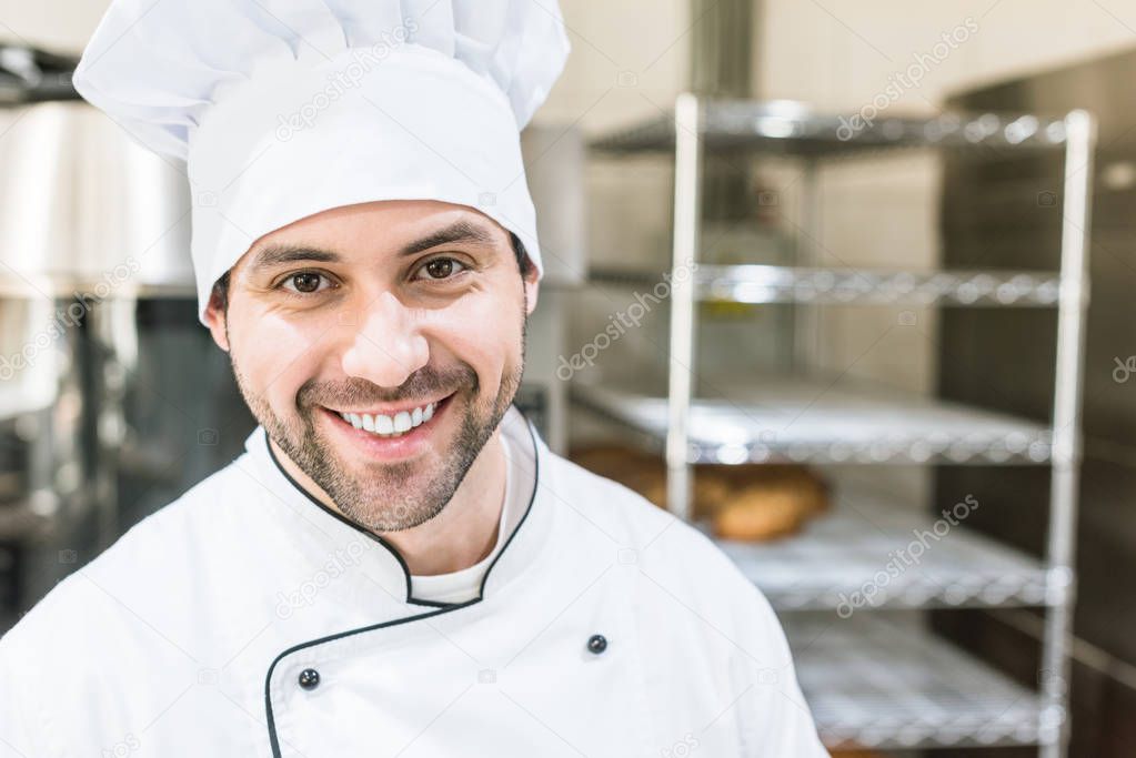 Handsome cook in chefs uniform smiling in bakehouse 