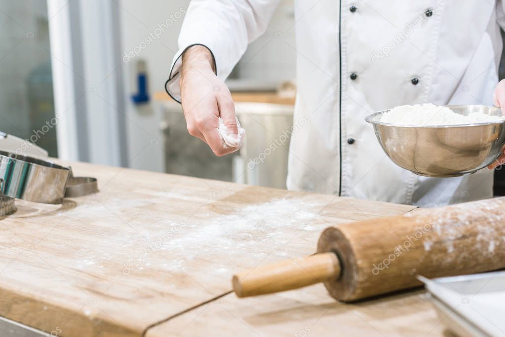 Cropped view of cook hands scattering flour on wooden table