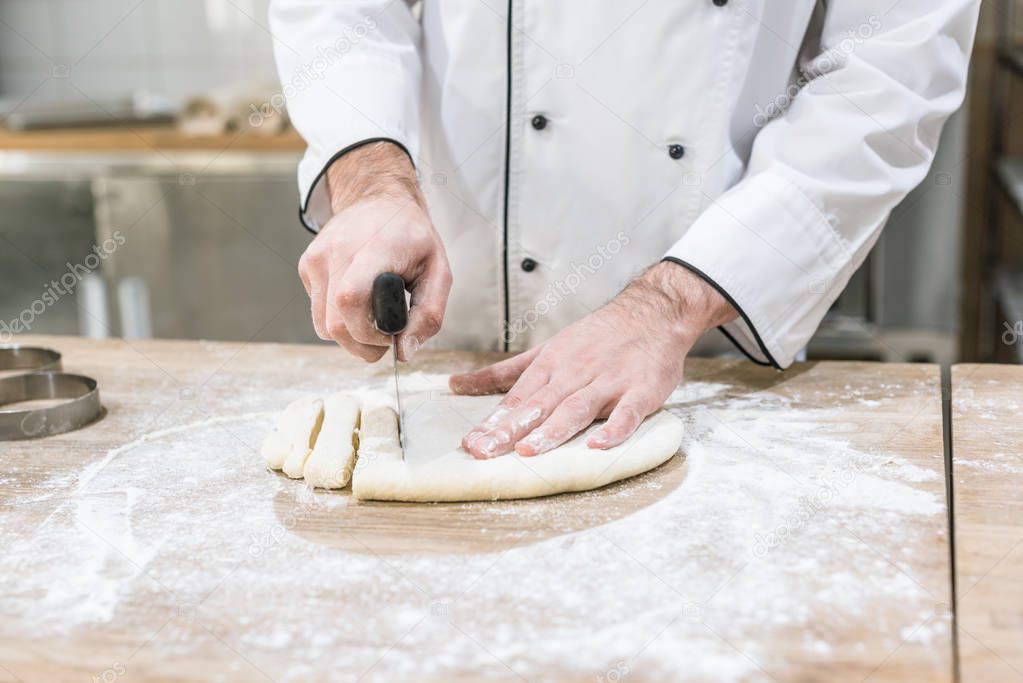 close up of baker hands cutting dough on wooden table