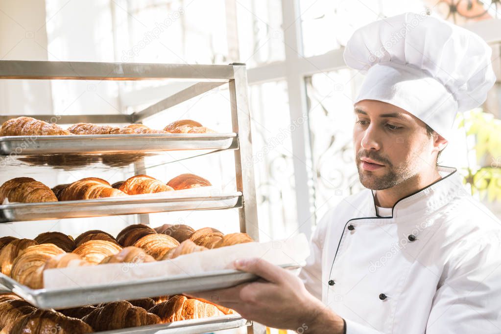 baker in chefs uniform looking at trays with fresh cooked croissants