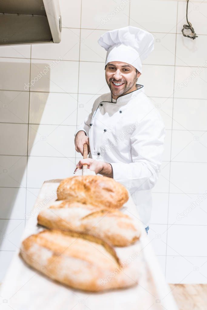 Smiling chef taking out loaves of bread in bakery