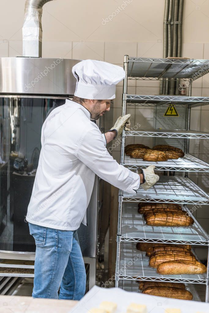 Side view of male chef holding rack with loaves of bread 