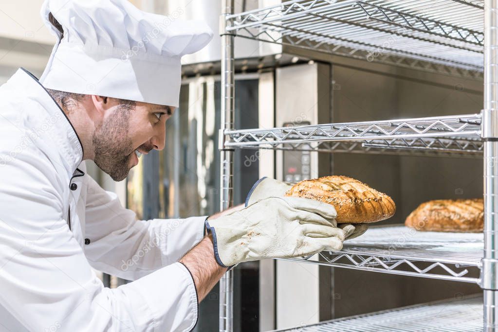 Side view of chef taking freshly baked bread from shelf 