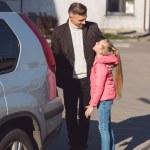 Tochter schaut Papa an und lächelt neben Auto