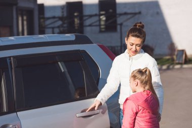 Mother opening car door and standing with daughter on street clipart