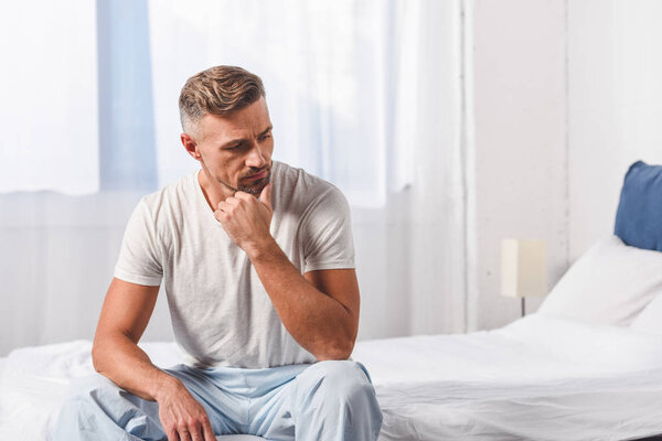 Thoughtful man sitting in pyjamas on bed 