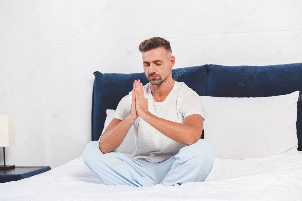Handsome man practising yoga on bed