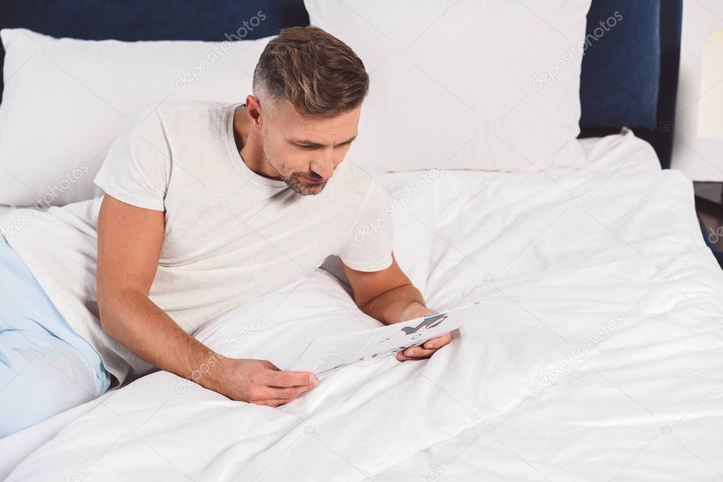 Handsome man reading newspaper in bedroom