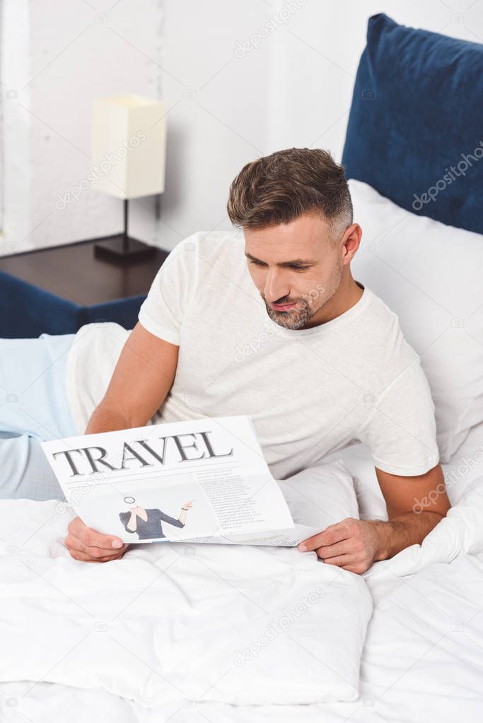 Handsome man reading travel newspaper in bed