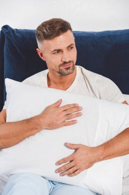 Handsome man holding pillow in room  clipart