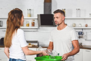 Yetişkin kadın boş plastik şişe koyarak mutfak at yeşil kutu geri dönüşüm