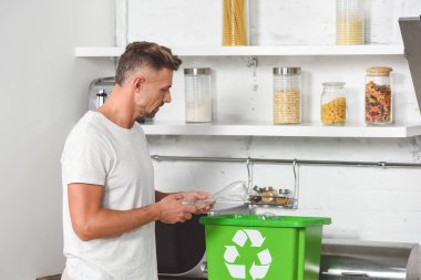 yetişkin adam boş plastik şişe yeşil geri dönüşüm kutusuna koyarak