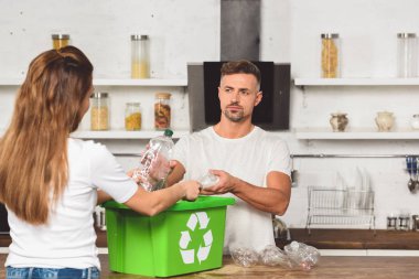 Plastik şişe alarak ve karısı geri dönüşüm kutusu mutfak masasında seyir yetişkin koca