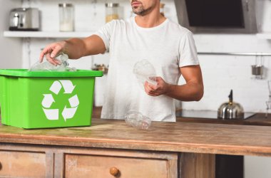 cropped vie of man putting plastic bottles in green recycle box clipart