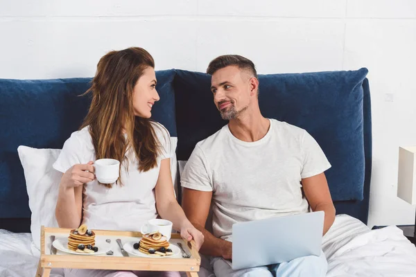 Esposo Mirando Esposa Sentado Con Ordenador Portátil Cama — Foto de stock gratis