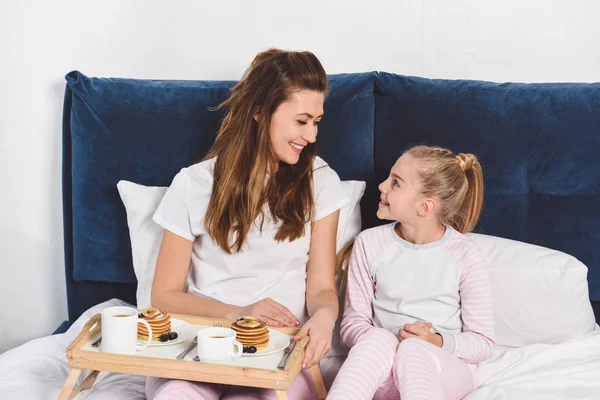 mother and daughter sitting in bed and having breakfast together
