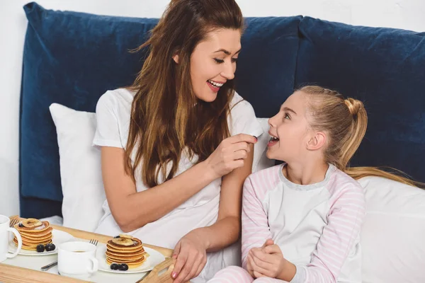 mother feeding daughter in bed during breakfast