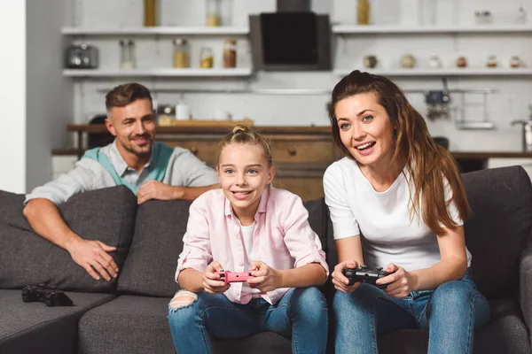 Sorrindo Mãe Filha Jogando Videogame Enquanto Pai Esconde Atrás Sofá — Fotografia de Stock