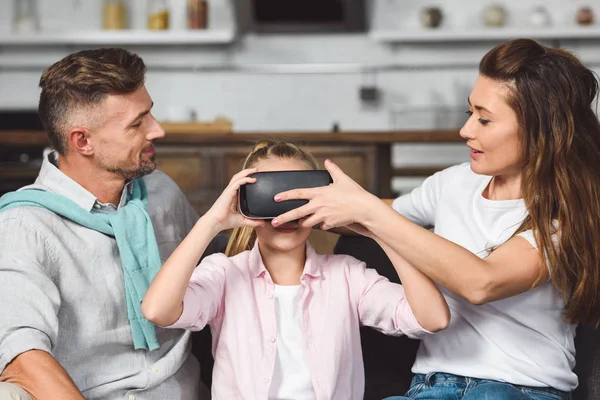 両親はソファーに座っていたと娘の頭の上の仮想現実ヘッドセットを入れて  — 無料ストックフォト