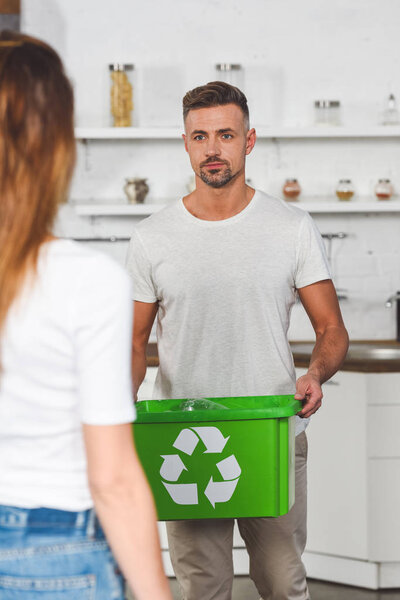 adult man holding green box with recycle sign and looking at woman 