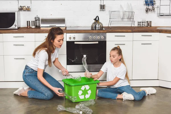 母と娘は台所の床に座って 空のペットボトルをリサイクル ボックスに入れて署名します — ストック写真