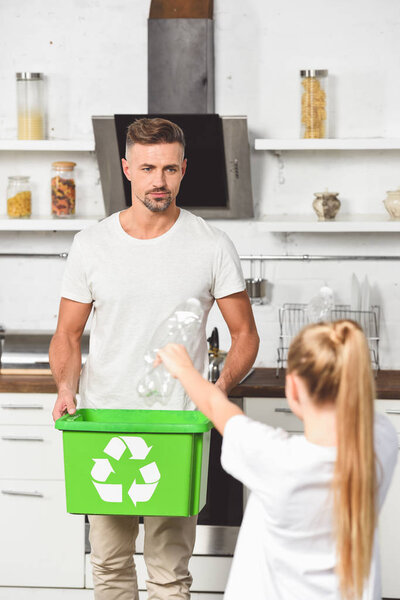 father holding green recycle box while daughter holding empty plastic bottles 