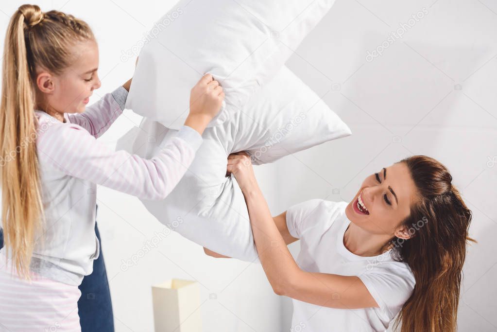 Cheerful mother and daughter having pillow fight at home 