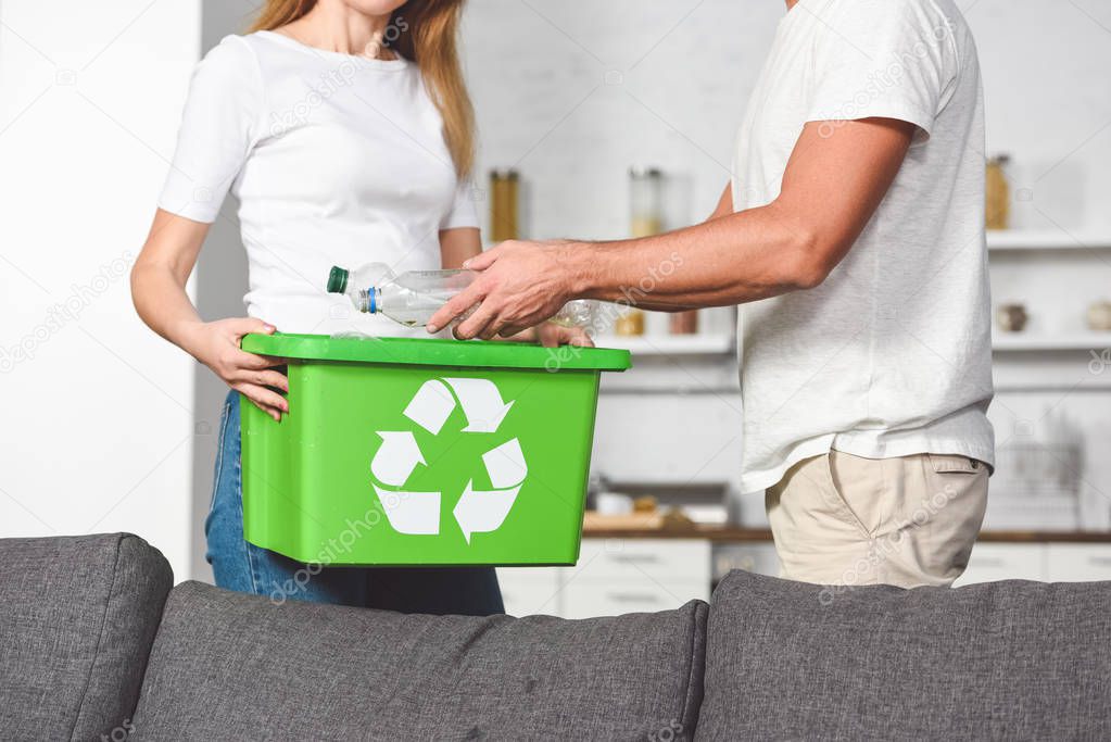 cropped view of adult couple putting empty plastic bottles in recycle green box