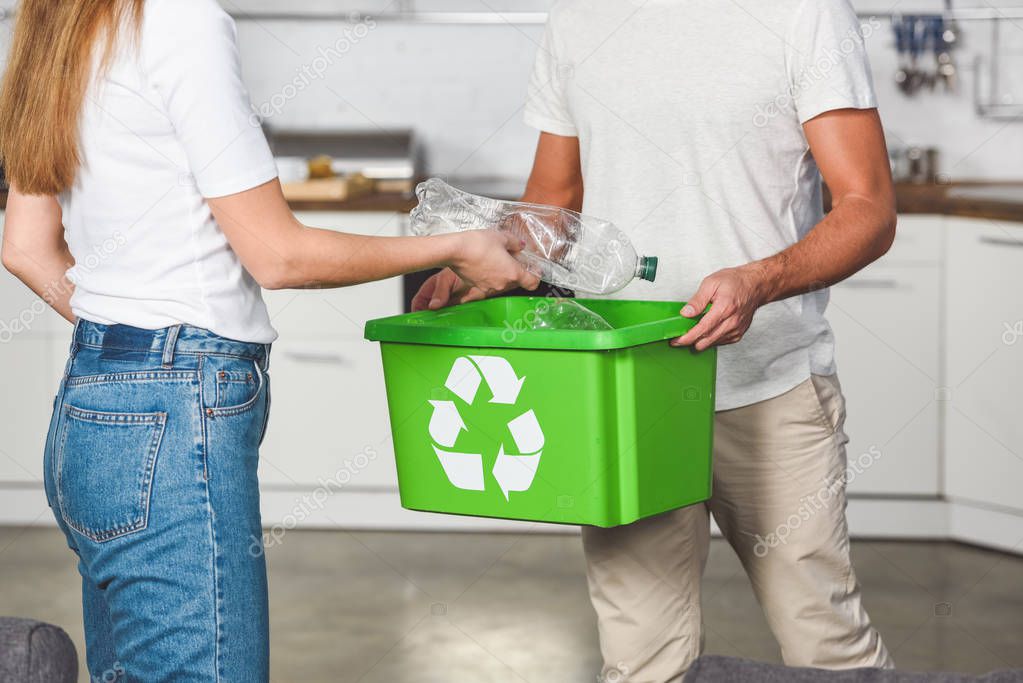 cropped view of woman putting empty plastic bottles in recycle green box 