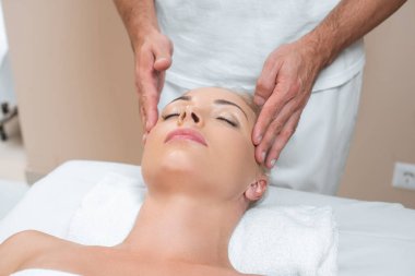 Erkek masör kadına spa salonda yüz masaj yapıyor 