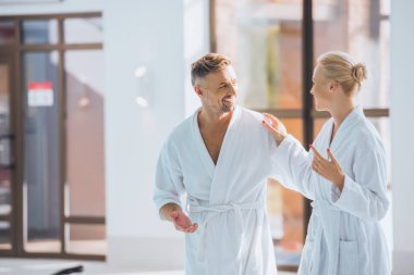 Yetişkin iki yürüme ve kaplıcada konuşurken beyaz bornoz içinde gülümseyen 