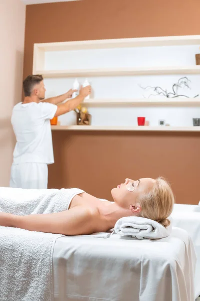 Massör Tar Flaskor Från Hyllan Medan Kvinnan Ligga Massagebänk — Stockfoto