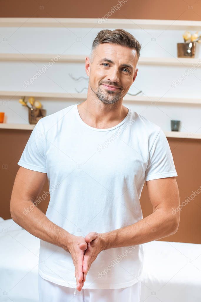 Handsome therapist warming hands in spa room 