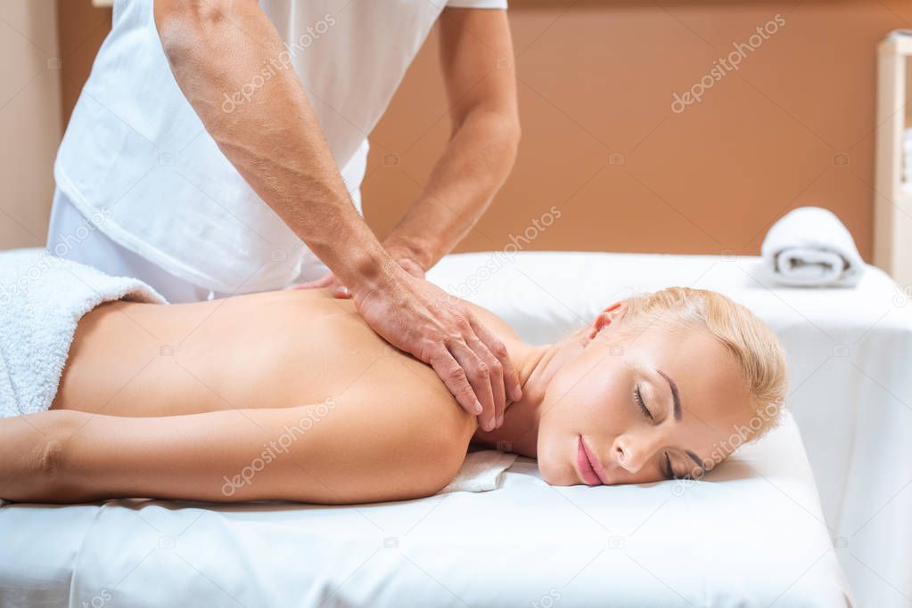 Blonde woman enjoying massage of male therapist in spa 