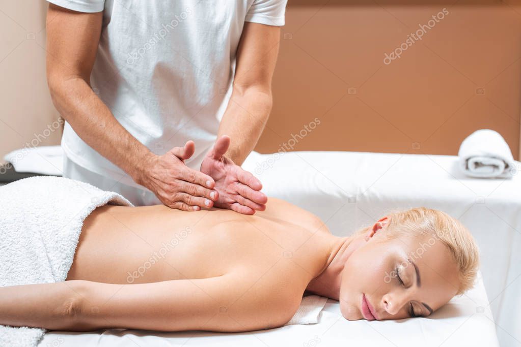 Male masseur doing back massage to woman in beauty salon 