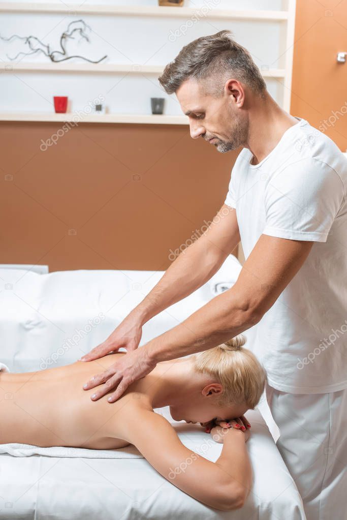 Handsome masseur doing massage of back to blonde woman